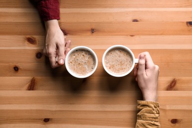 Women with cups of coffee at wooden table, top view