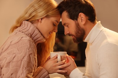 Photo of Lovely couple with cuphot drink spending time together near fireplace at home