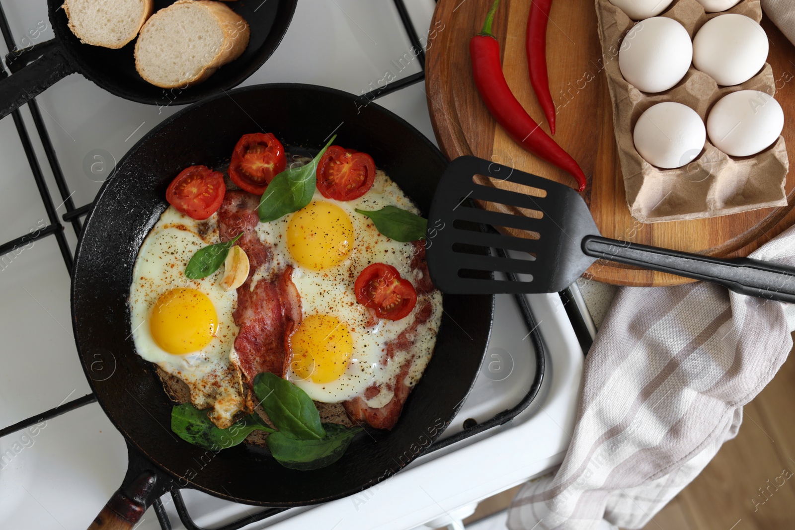 Photo of Delicious fried eggs with bacon and tomatoes in pan on stove, top view