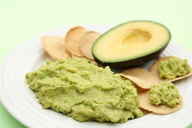 Delicious guacamole, avocado and chips on light green background, closeup