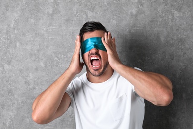 Photo of Emotional young man wearing light blue blindfold on grey background