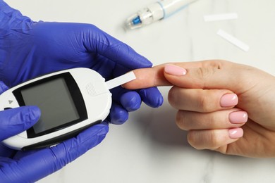 Photo of Diabetes. Doctor checking patient's blood sugar level with glucometer at white table, closeup