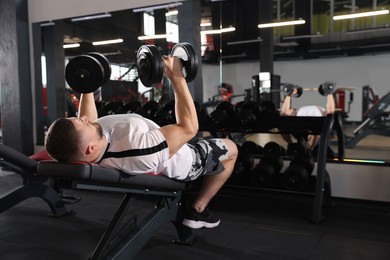 Athletic man training with dumbbells in gym