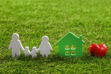 Photo of Figures of family, red heart and house on green grass