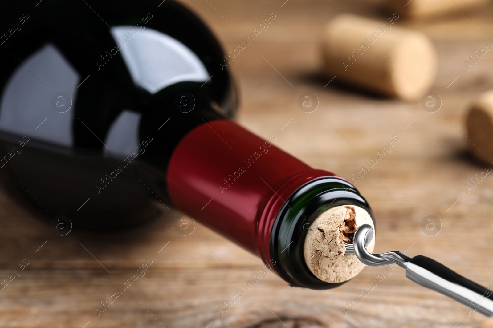 Photo of Opening wine bottle with corkscrew on wooden table, closeup