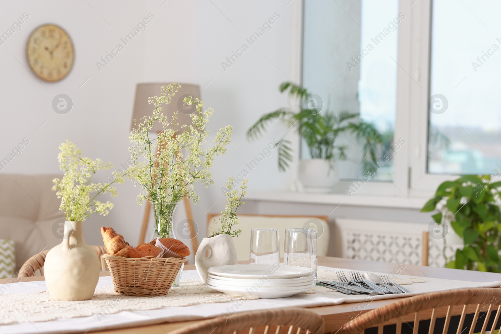 Photo of Clean dishes, flowers and fresh pastries on table in stylish dining room