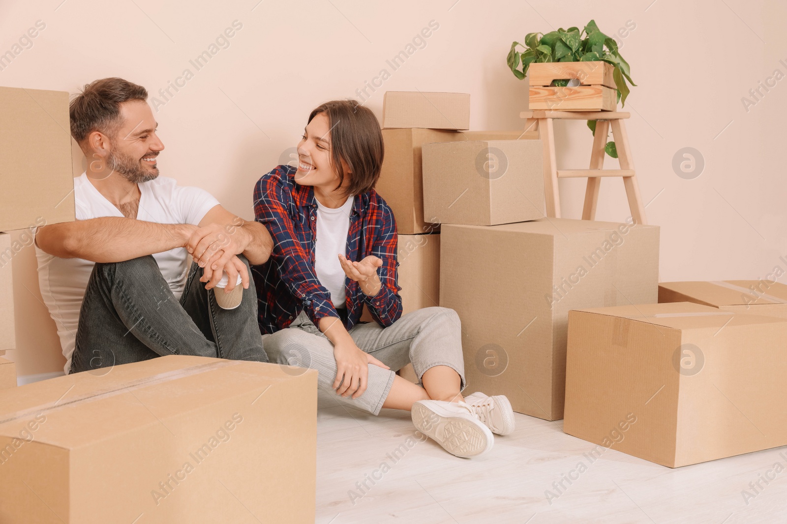 Photo of Happy couple with takeaway coffee resting on floor in new apartment. Moving day