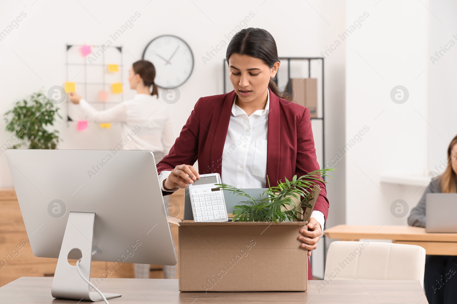 Photo of Unemployment problem. Woman with box of personal belongings at table in office