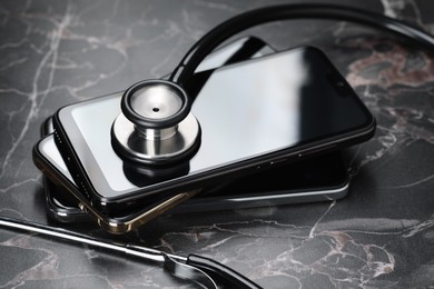 Photo of Stack of modern smartphones and stethoscope on black table