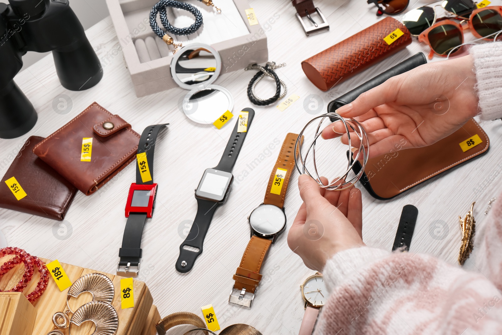 Photo of Woman holding metal earrings near table with different stuff, closeup. Garage sale