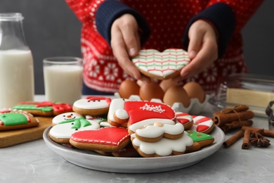 Photo of Woman holding delicious homemade Christmas cookie at grey marble table, focus on plate