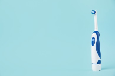 Photo of Electric toothbrush on light blue background, space for text