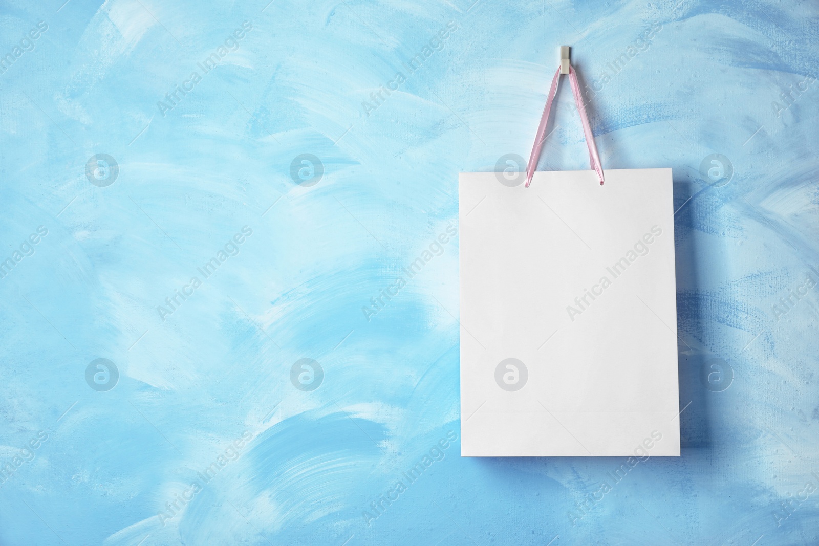 Photo of Paper shopping bag with ribbon handles hanging on color wall. Mockup for design