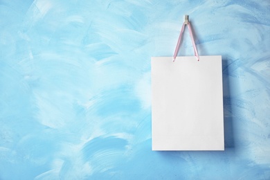 Paper shopping bag with ribbon handles hanging on color wall. Mockup for design