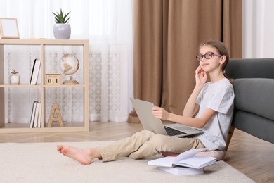 Photo of Thoughtful girl with laptop and books on floor at home