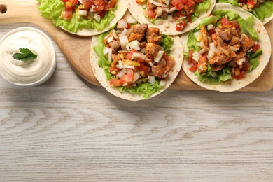 Delicious tacos with vegetables, meat and sauce on white wooden table, top view. Space for text