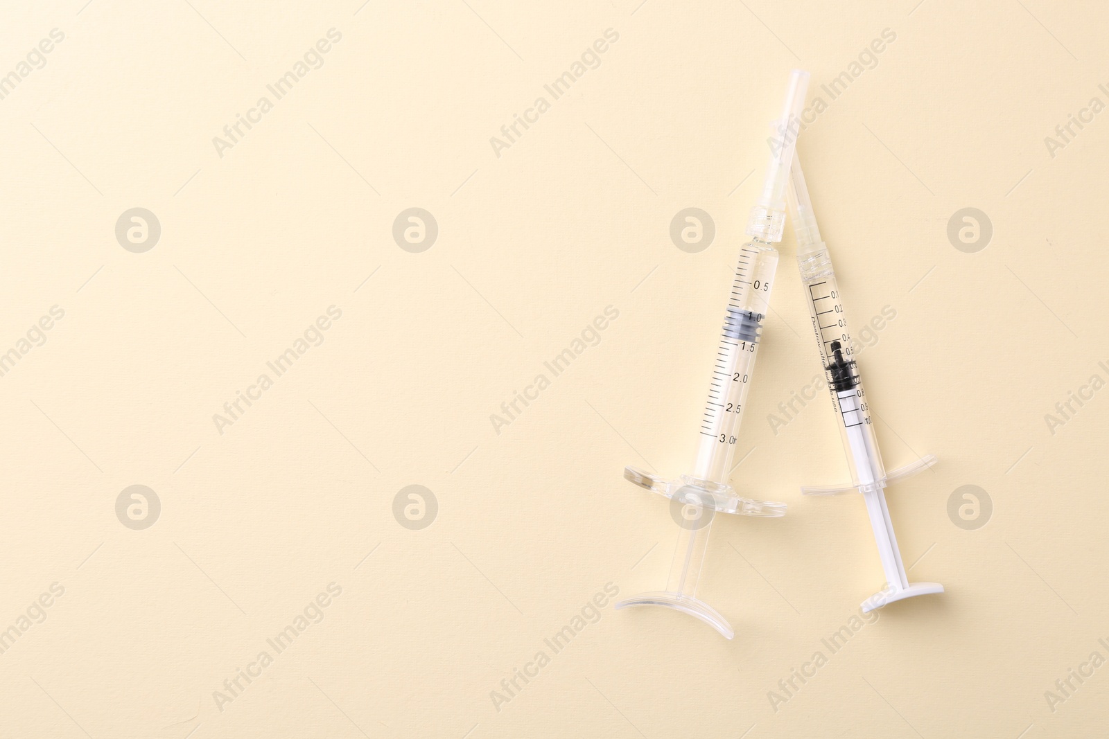 Photo of Injection cosmetology. Two medical syringes on beige background, top view. Space for text