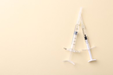 Photo of Injection cosmetology. Two medical syringes on beige background, top view. Space for text