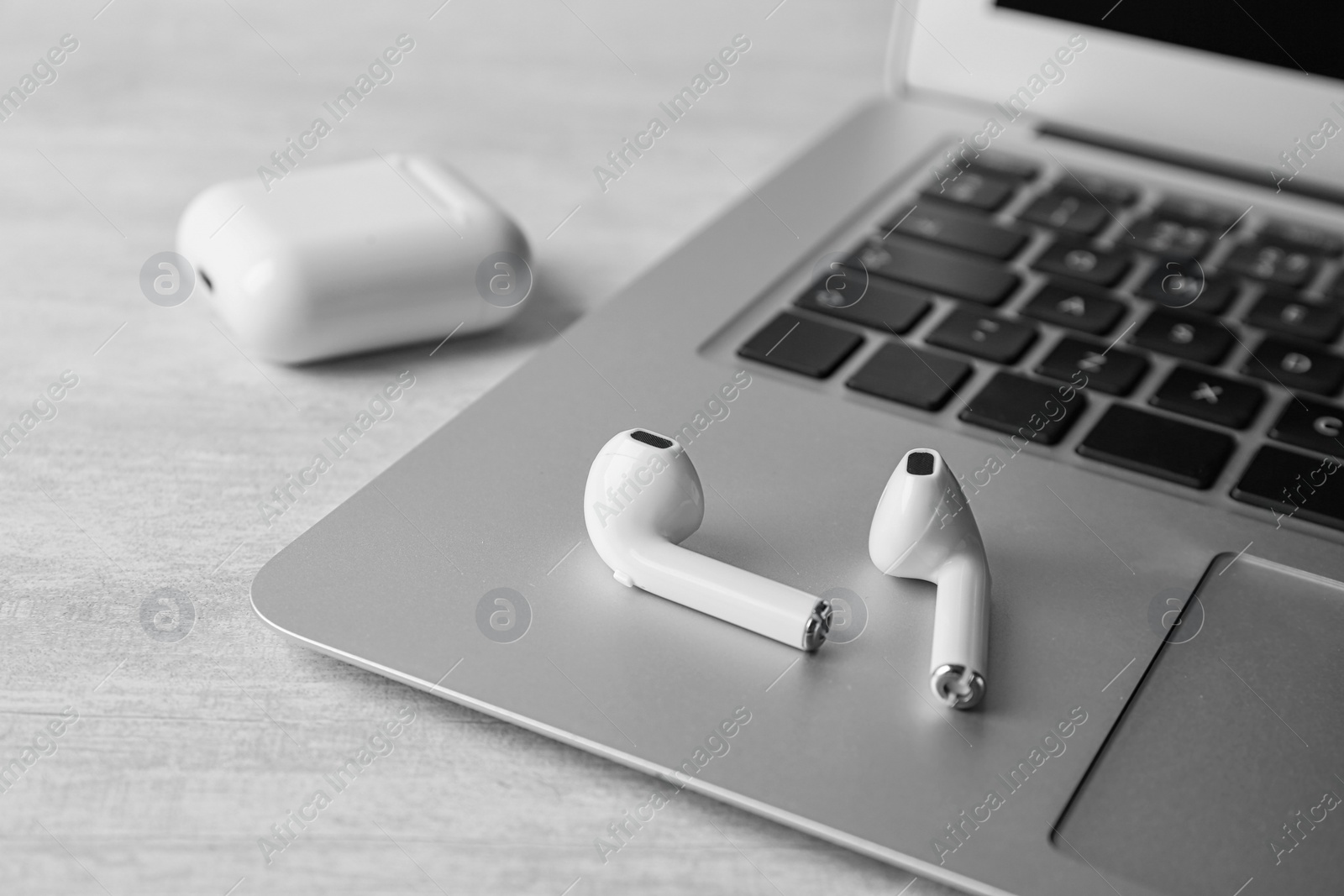 Photo of Modern wireless earphones and laptop on light table