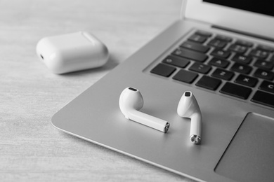 Photo of Modern wireless earphones and laptop on light table