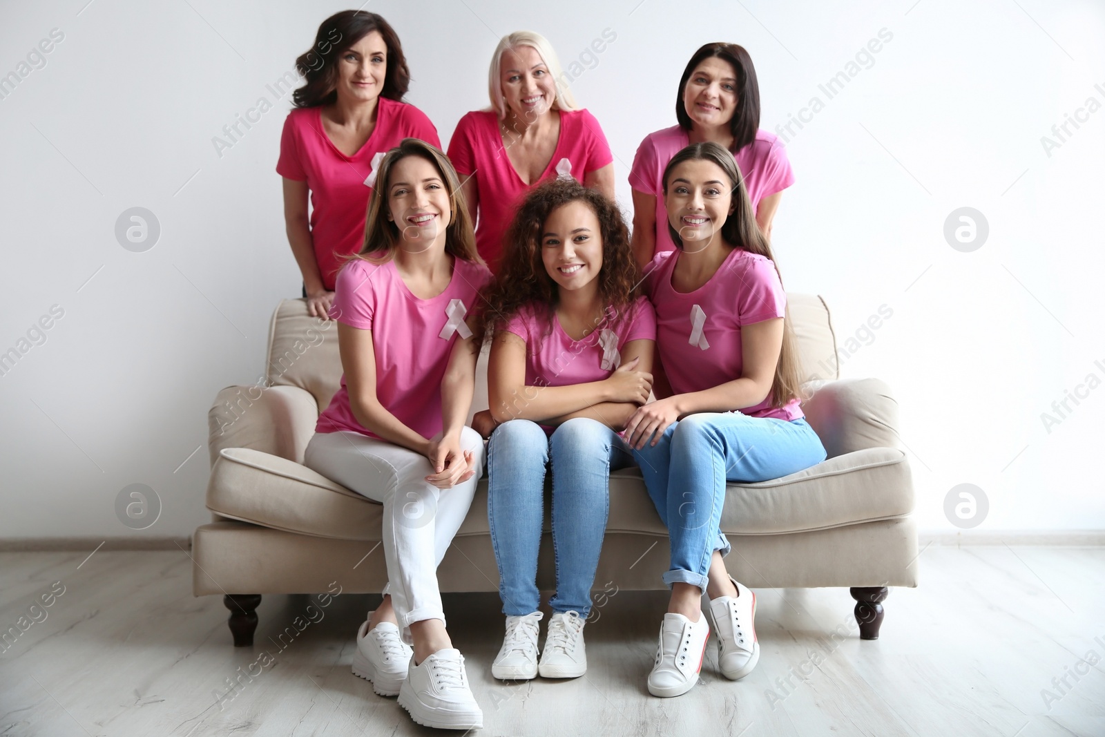 Photo of Group of women with silk ribbons on sofa near light wall. Breast cancer awareness concept