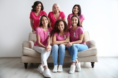 Group of women with silk ribbons on sofa near light wall. Breast cancer awareness concept