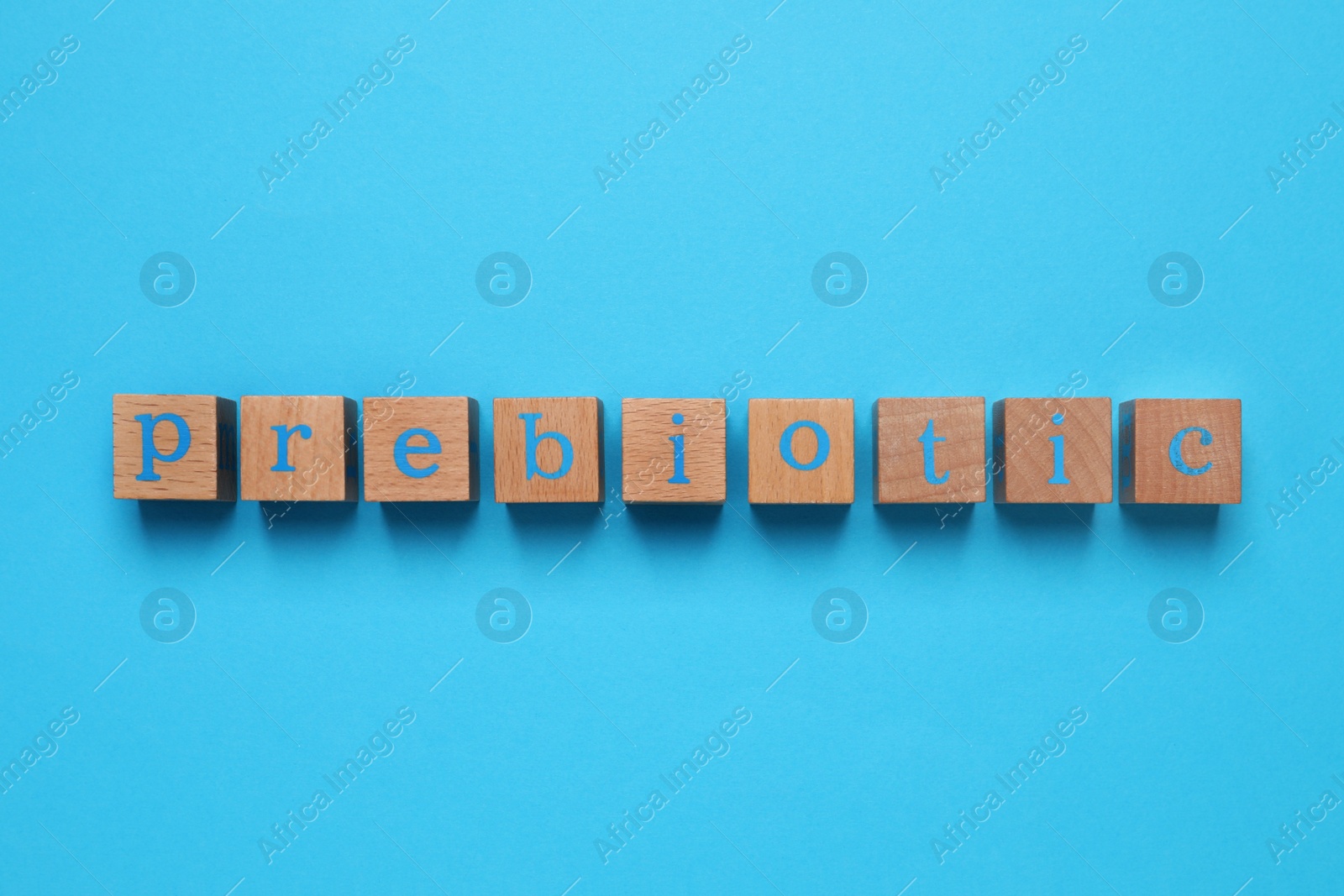 Photo of Wooden cubes with word Prebiotic on light blue background, flat lay