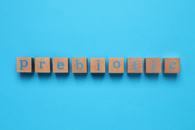 Wooden cubes with word Prebiotic on light blue background, flat lay