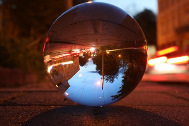Photo of Beautiful city street, overturned reflection. Crystal ball on asphalt road at night, closeup