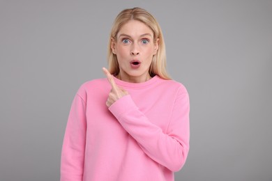 Surprised woman pointing at something on grey background