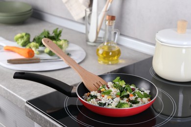 Frying tasty rice with vegetables on induction stove in kitchen