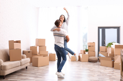 Photo of Happy couple having fun in room with cardboard boxes on moving day
