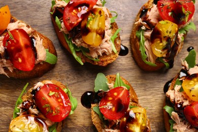 Delicious bruschettas with balsamic vinegar, tomatoes, arugula and tuna on wooden table, flat lay