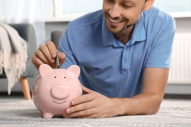 Photo of Happy man putting money into piggy bank at home, closeup
