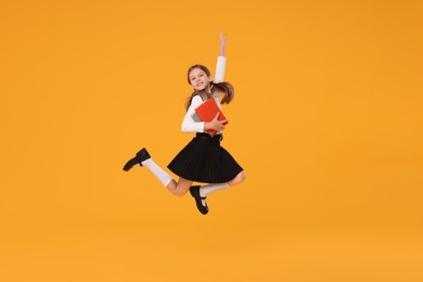 Photo of Happy schoolgirl with books jumping on orange background