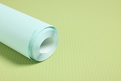 Photo of One light turquoise wallpaper roll on green sample, space for text