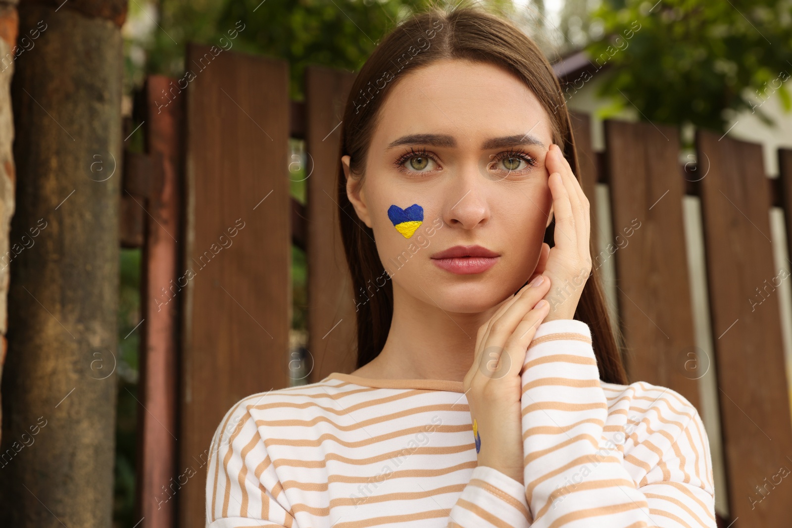 Photo of Young woman with drawing of Ukrainian flag on face outdoors