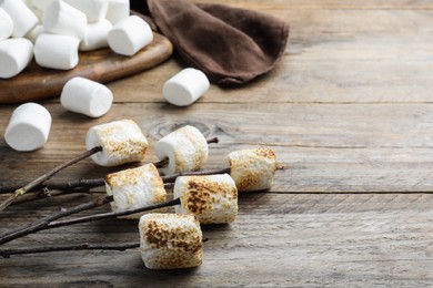 Twigs with roasted marshmallows on wooden table, space for text