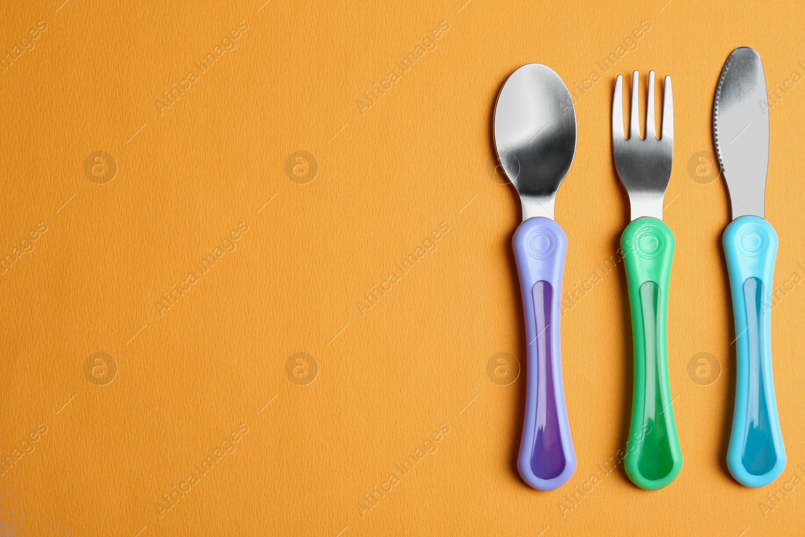 Photo of Set of small cutlery on orange background, flat lay with space for text. Serving baby food