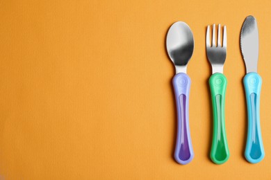 Photo of Set of small cutlery on orange background, flat lay with space for text. Serving baby food