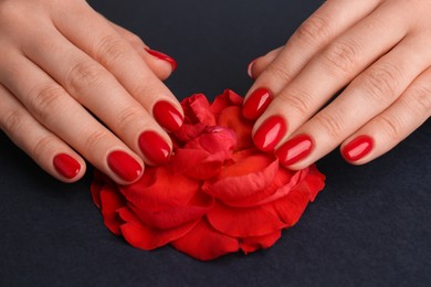 Photo of Woman with red polish on nails touching flower on black background, closeup