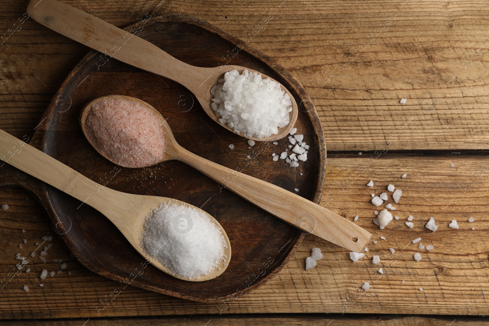 Photo of Different natural salt in spoons on wooden table, flat lay. Space for text