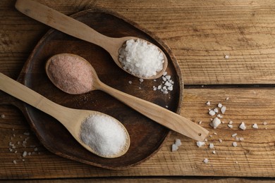 Photo of Different natural salt in spoons on wooden table, flat lay. Space for text