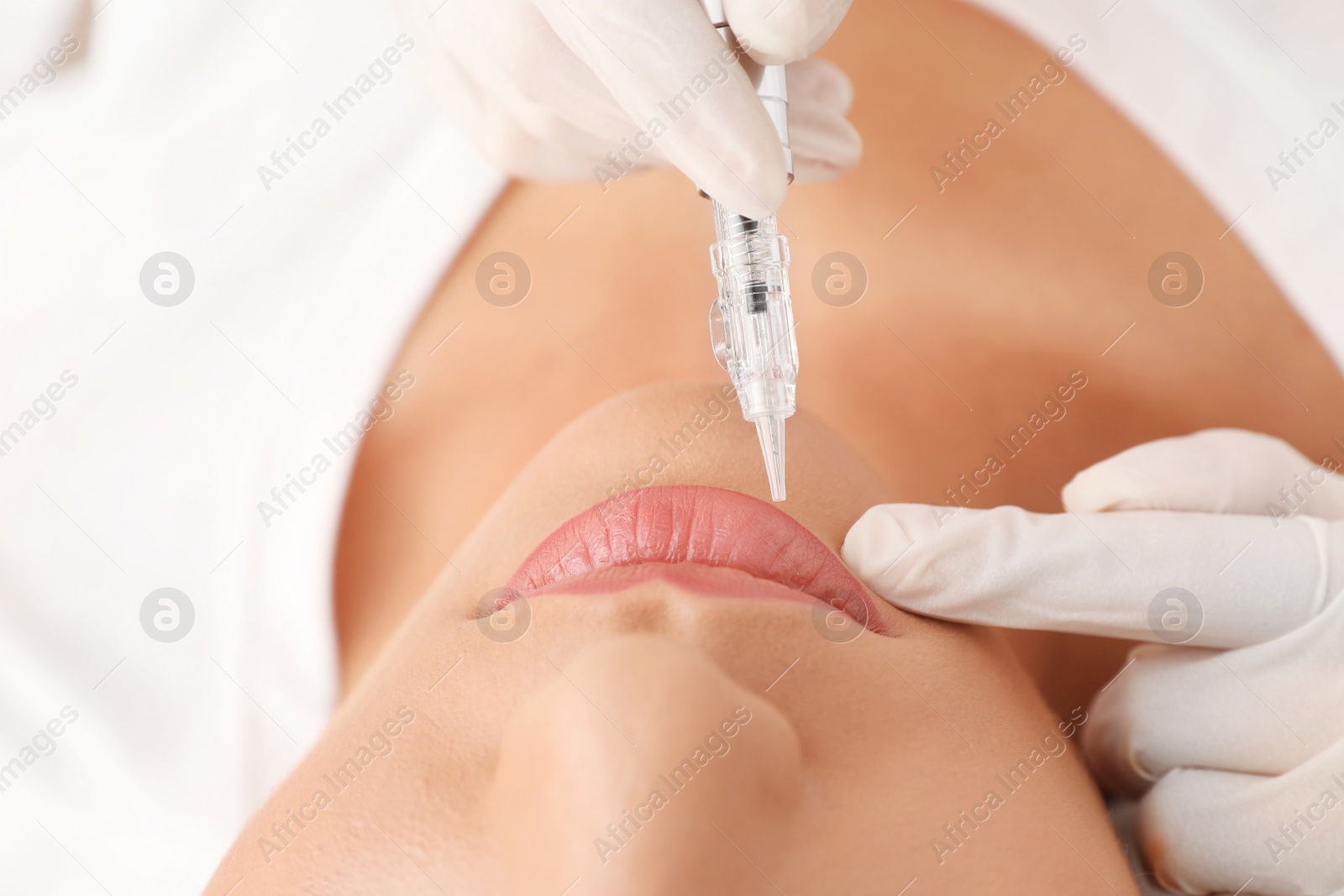 Photo of Young woman undergoing procedure of permanent lip makeup in tattoo salon, closeup