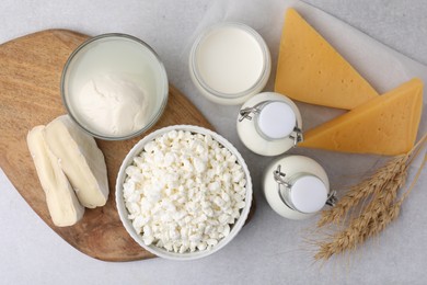 Different fresh dairy products and wheat ears on light table, flat lay