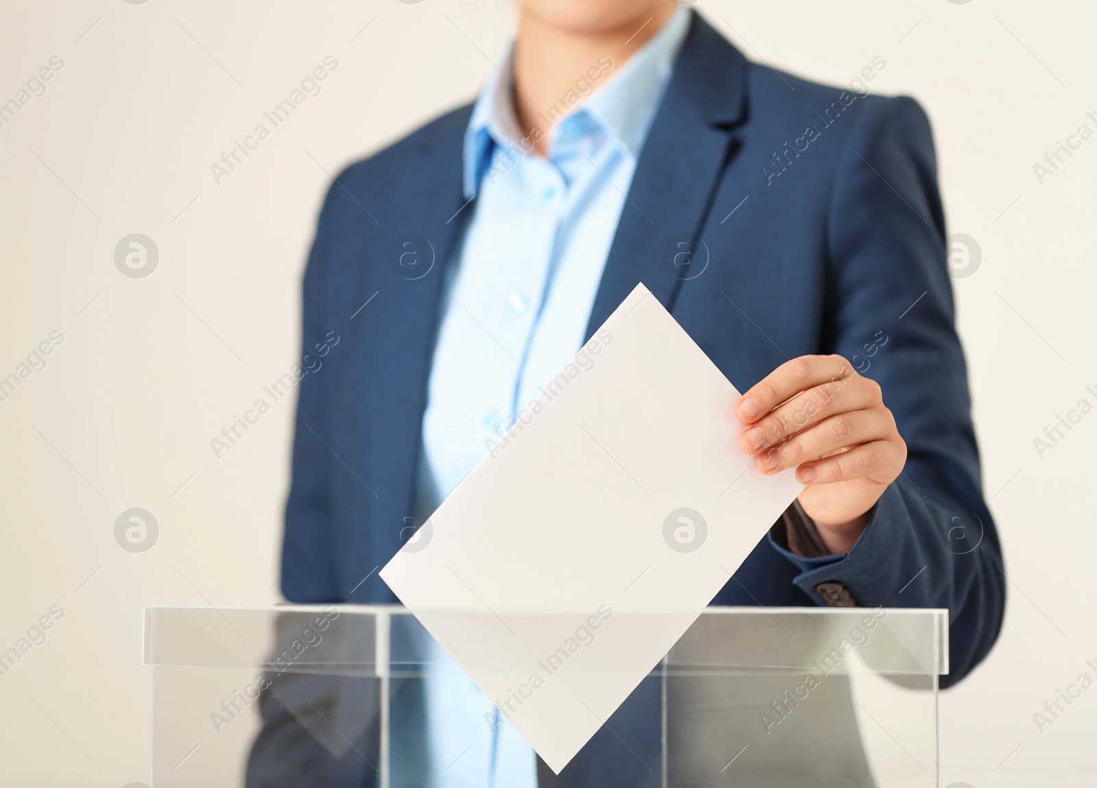Photo of Woman putting vote into ballot box against light background, closeup