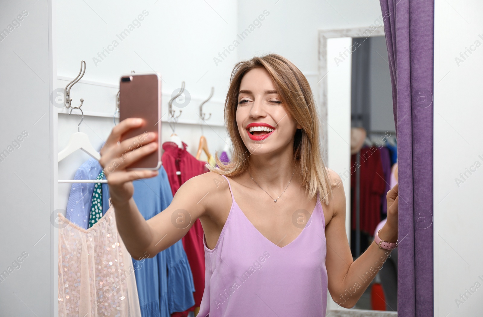 Photo of Young woman taking selfie in dressing room. Fashion store