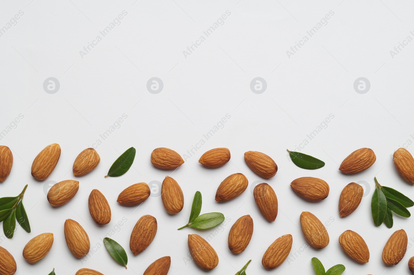 Photo of Delicious almonds and fresh leaves on white background, flat lay. Space for text