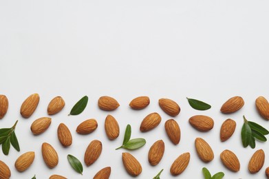 Delicious almonds and fresh leaves on white background, flat lay. Space for text
