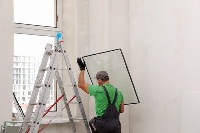 Photo of Worker in uniform holding double glazing window indoors, back view